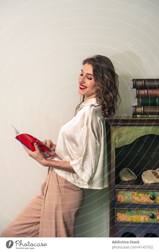 Junge Frau mit Buch steht in der Nähe von Vintage-Möbel lesen altehrwürdig retro Stil Glück Lächeln jung positiv sich[Akk] entspannen Hobby ruhen Etage