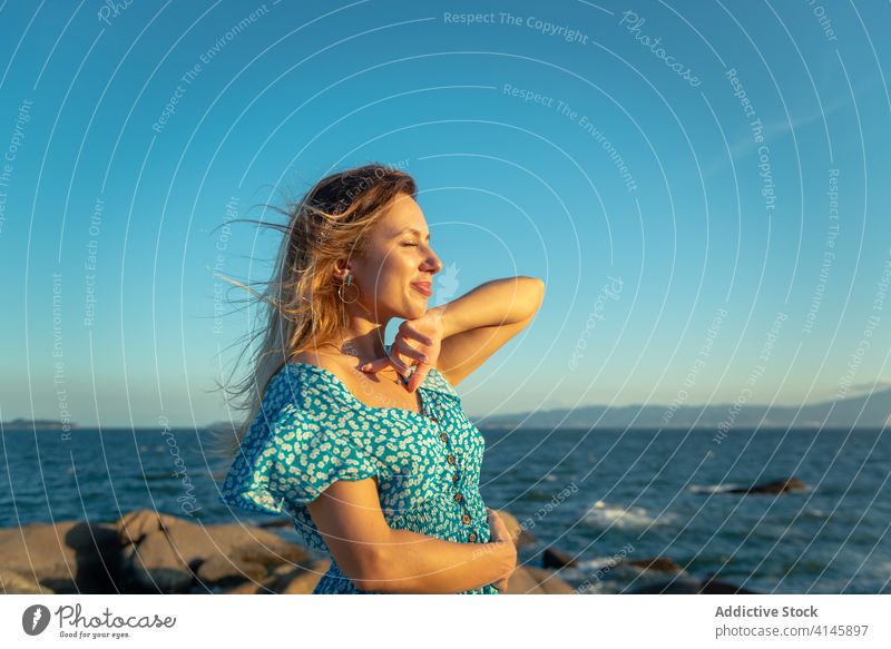 Lächelnde junge Touristin erholt sich bei Sonnenuntergang im ruhigen Meer Frau Erholung Meeresufer Augen geschlossen genießen Glück Reisender Sommer Urlaub