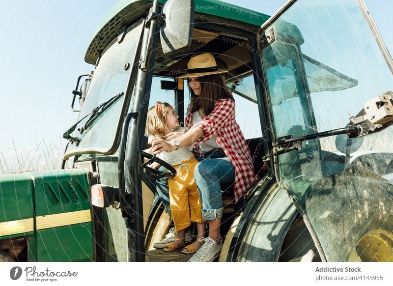 Glückliche Frau umarmt kleines Kind sitzt in Traktor auf dem Lande Mutter Umarmen Tochter Kinderbetreuung Zuneigung Bonden Landschaft Zeit verbringen