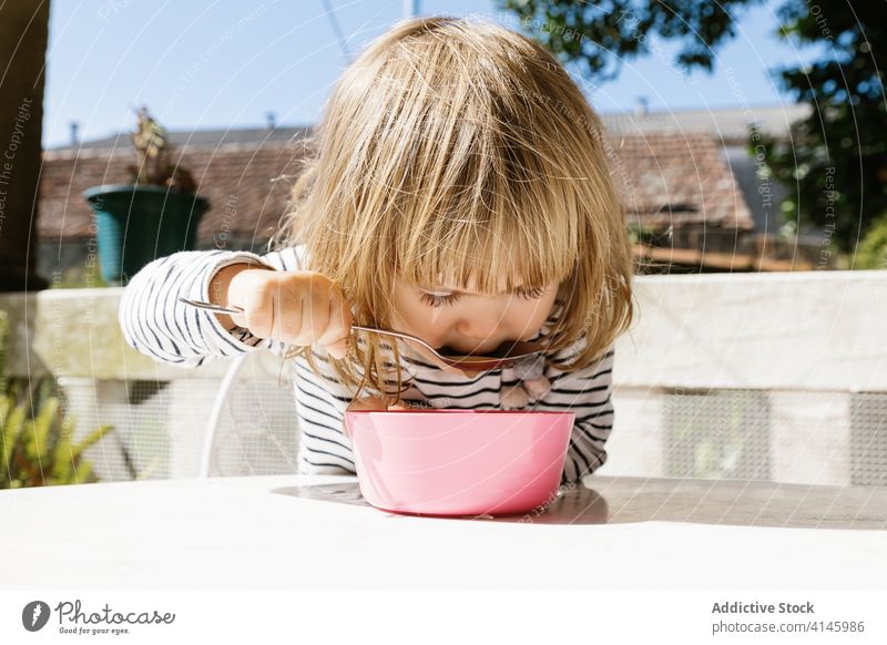 Charmantes Mädchen sitzt am Tisch beim Frühstück bezaubernd Kind Morgen Terrasse Lächeln Lebensmittel Schalen & Schüsseln Glück sitzen sich[Akk] entspannen