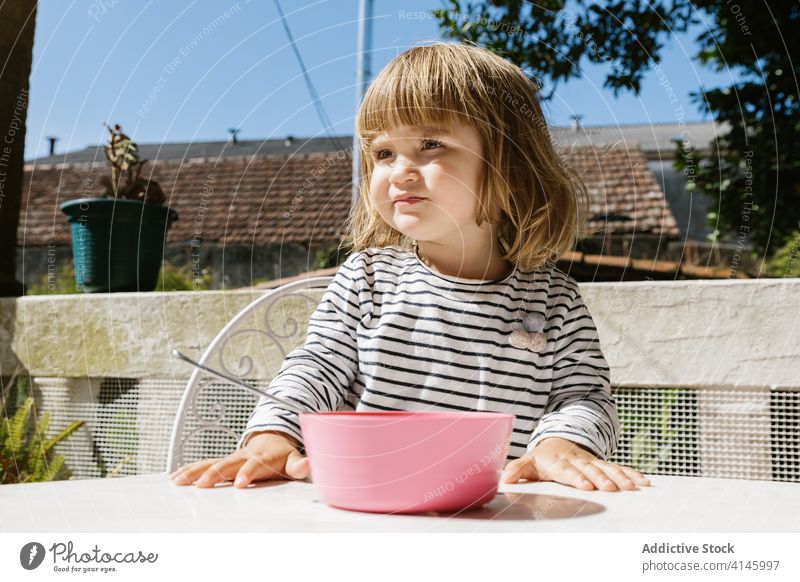 Charmantes Mädchen sitzt am Tisch beim Frühstück bezaubernd Kind Morgen Terrasse Lächeln Lebensmittel Schalen & Schüsseln Glück sitzen sich[Akk] entspannen