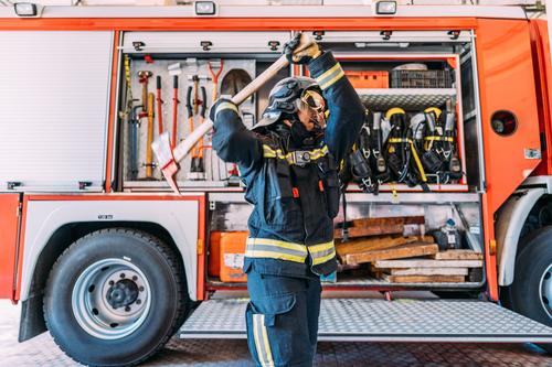 Anonymer Feuerwehrmann mit alter Spitzhacke in der Nähe eines Feuerwehrwagens führen Uniform Gerät Pickel Lastwagen Werkzeug Arbeit Sicherheit Weste Instrument