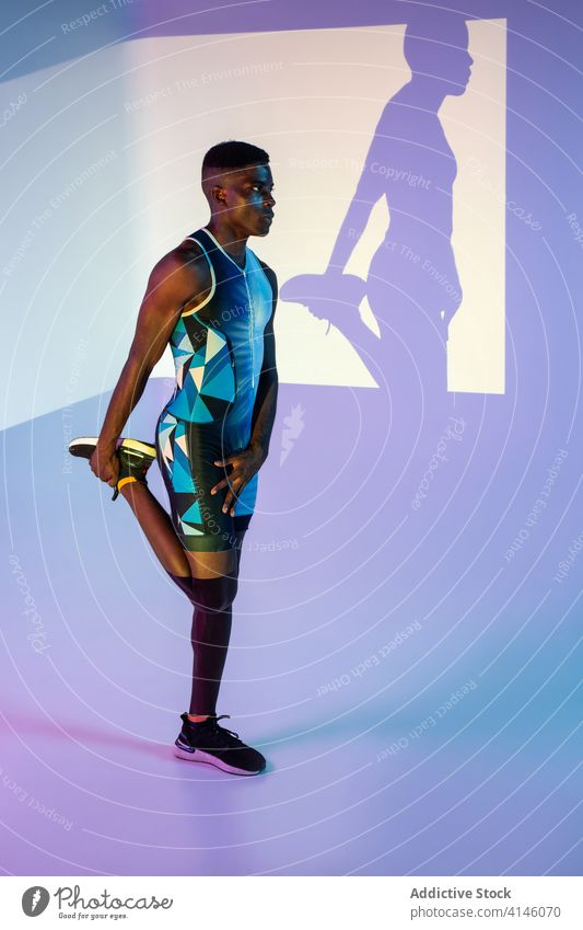 Schwarzer Athlet beim Training im Neonlicht Sportler Übung Mann Energie stark neonfarbig Dehnung Beine ernst Aufwärmen ausführen üben brutal Bestimmen Sie aktiv