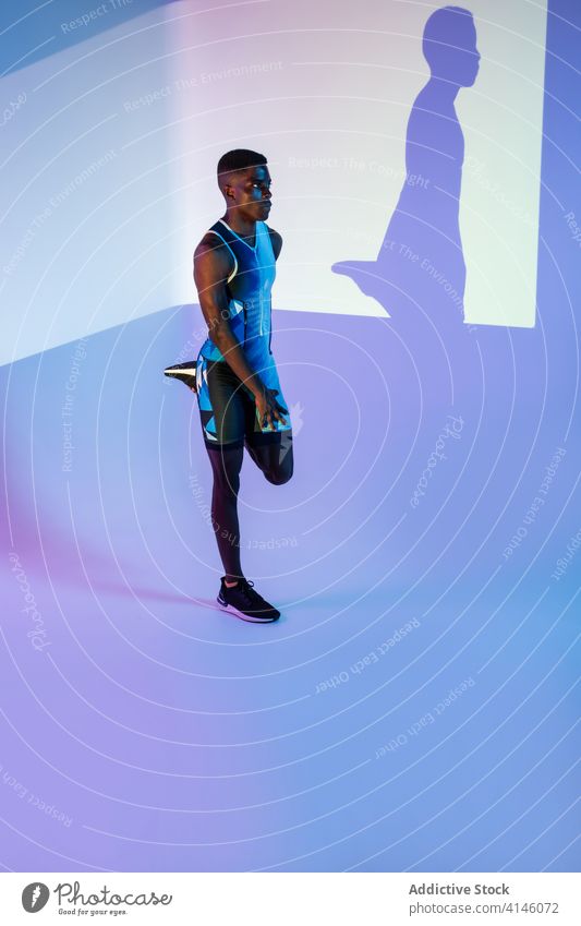 Schwarzer Athlet beim Training im Neonlicht Sportler Übung Mann Energie stark neonfarbig Dehnung Beine ernst Aufwärmen ausführen üben brutal Bestimmen Sie aktiv