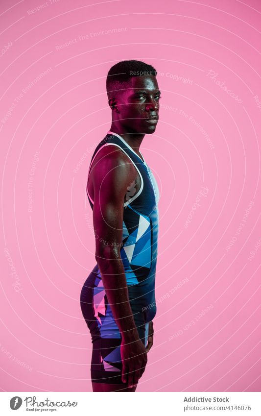 Schwarzer Athlet beim Training im Neonlicht Sportler Übung Mann stehen Energie stark neonfarbig ernst ausführen üben brutal in die Kamera schauen Bestimmen Sie