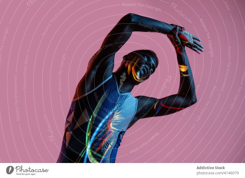 Schwarzer Athlet beim Training im Neonlicht Sportler Übung Wegbiegung Mann Energie stark neonfarbig Dehnung ernst Aufwärmen ausführen üben brutal Bestimmen Sie