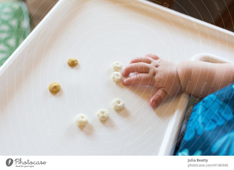 Smiley-Gesicht aus Getreideflocken und Joghurttropfen auf einem Hochstuhltablett; Baby streckt die Hand aus, um sich selbst zu füttern Säugling Kind