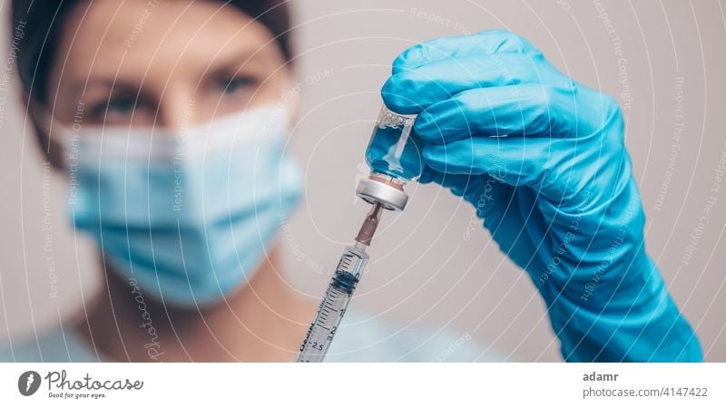 Arzt in Schutzhandschuhen und Maske hält Glasfläschchen mit Injektionsflüssigkeit. Impfung gegen Influenza und Coronavirus. Impfstoff Medizin Einspritzung