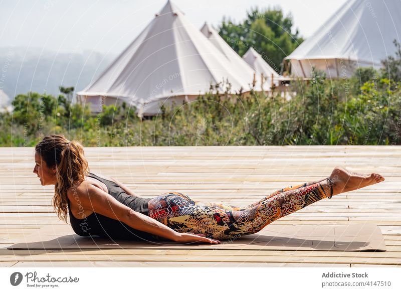 Konzentrierte Frau beim Heuschrecken-Asana während einer Yoga-Sitzung im Freien salabhasana Lager Stressabbau Dehnung Gleichgewicht Wellness üben hölzern Podest