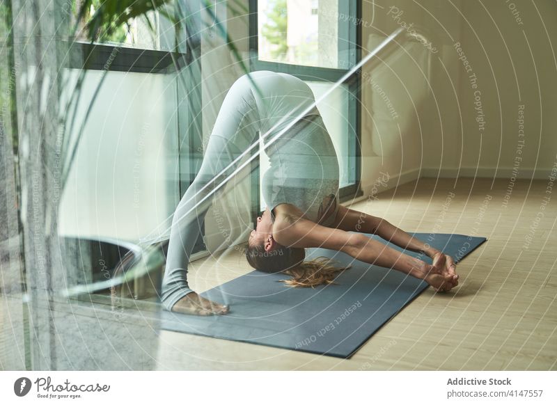 Starke Sportlerin bei einer schwierigen Variation der Yoga-Pose "Weitbeinige Vorwärtsbeuge Frau Stärke Körper prasarita padottanasana c Atelier üben