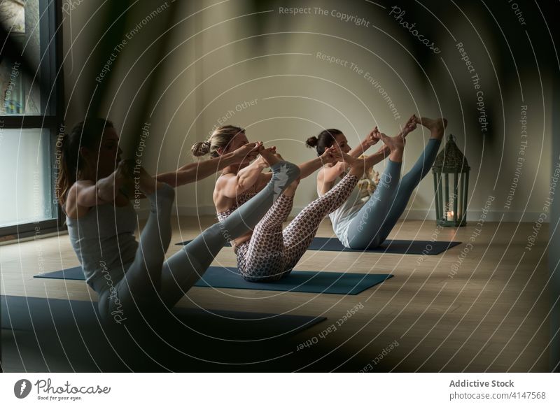 Fitte Sportlerinnen beim Dehnen und Ausgleichen von Asanas während einer Yoga-Sitzung Frauen üben Gleichgewicht Dehnung Boot mit doppeltem Zehengriff Lektion