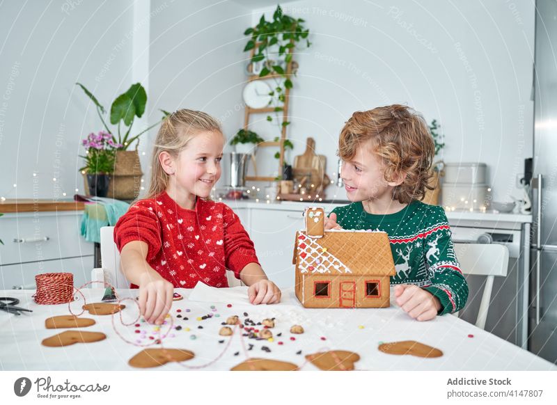 Glückliche Kinder bauen Lebkuchenhäuser Haus Weihnachten vorbereiten machen Zusammensein heiter heimwärts Küche Geschwisterkind wenig Lächeln Winter festlich