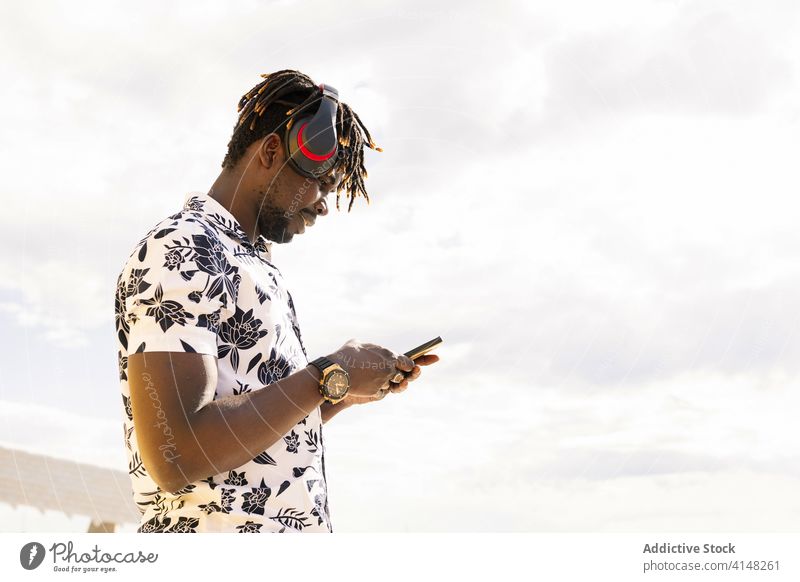 junger schwarzer Mann mit Kopfhörern schaut auf sein Handy Person Telefon Afrikanisch männlich Musik Amerikaner Technik & Technologie Mobile hören Mitteilung