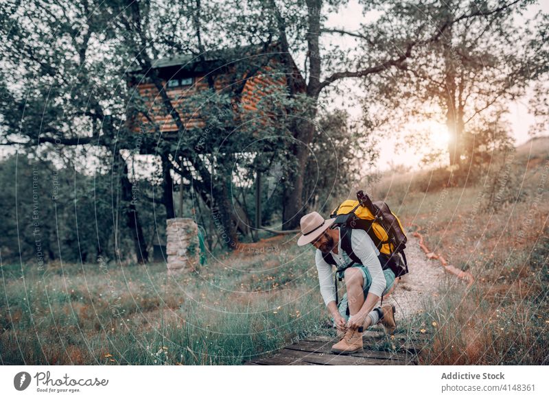 Männlicher Tourist mit Rucksack beim Schnürsenkelbinden Reisender Wald Mann Krawatte Schuhbänder Trekking Weg hölzern Backpacker Natur männlich Abenteuer reisen