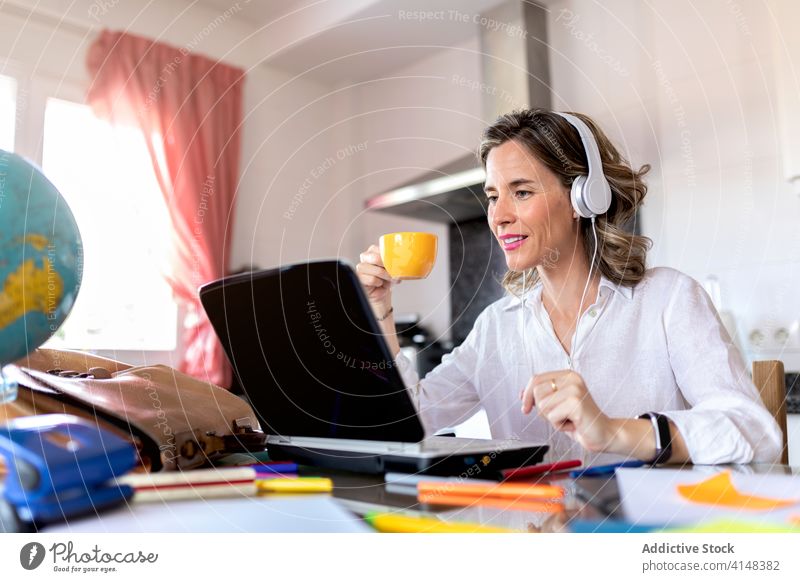 Positive Frau in Headset mit Videoanruf auf Laptop drinnen Tasse Heißgetränk Freizeit sprechen Lächeln benutzend Apparatur Gerät Netbook Gespräch Video-Chat
