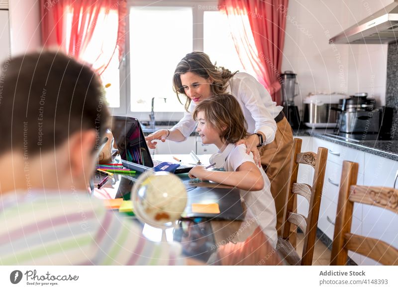 Mutter mit Junge beobachtet Laptop in der Nähe von unkenntlichem Geschwisterkind in der Küche Hausaufgabe Bildung interagieren teilen Kinderbetreuung Sohn