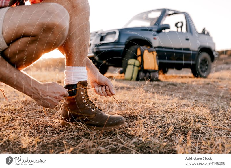 Gesichtsloser männlicher Reisender, der auf verblasstem Gras die Schnürsenkel seiner Stiefel bindet Tourist Krawatte Schuhbänder Urlaub Harmonie Automobil