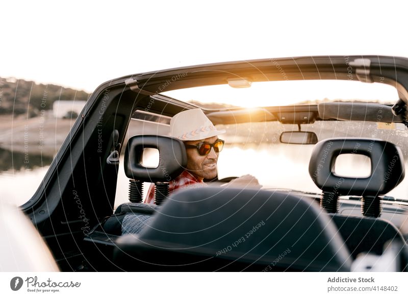 Lächelnder männlicher Reisender fährt Auto in der Nähe eines Sees im Sonnenschein Tourist Laufwerk PKW Urlaub Berge u. Gebirge Natur Wochenende Inhalt