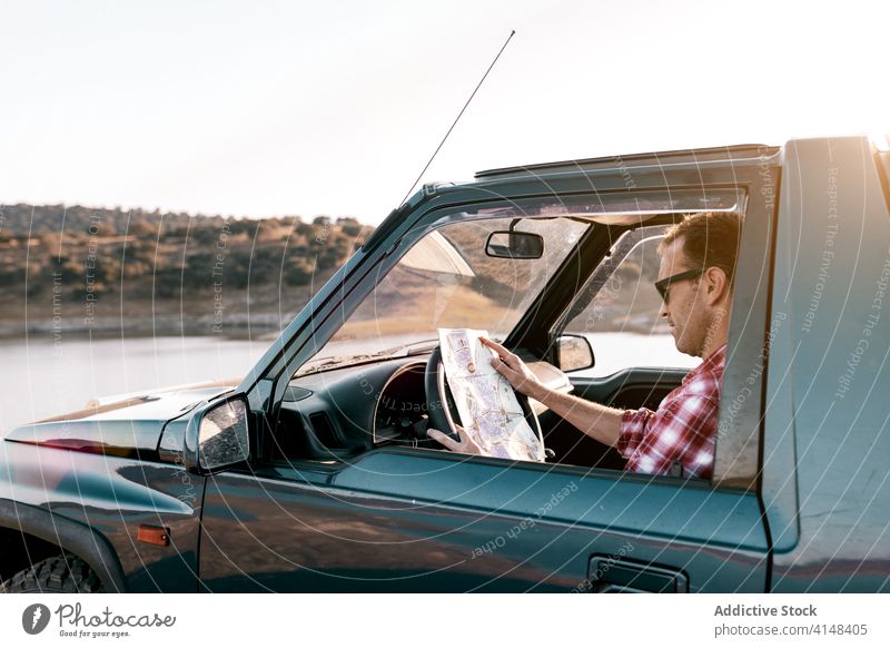 Unbekannter Tourist schaut auf eine Karte im Auto, das in der Nähe eines Sees geparkt ist zuschauen Landkarte Ausflugsziel navigieren Route Urlaub PKW