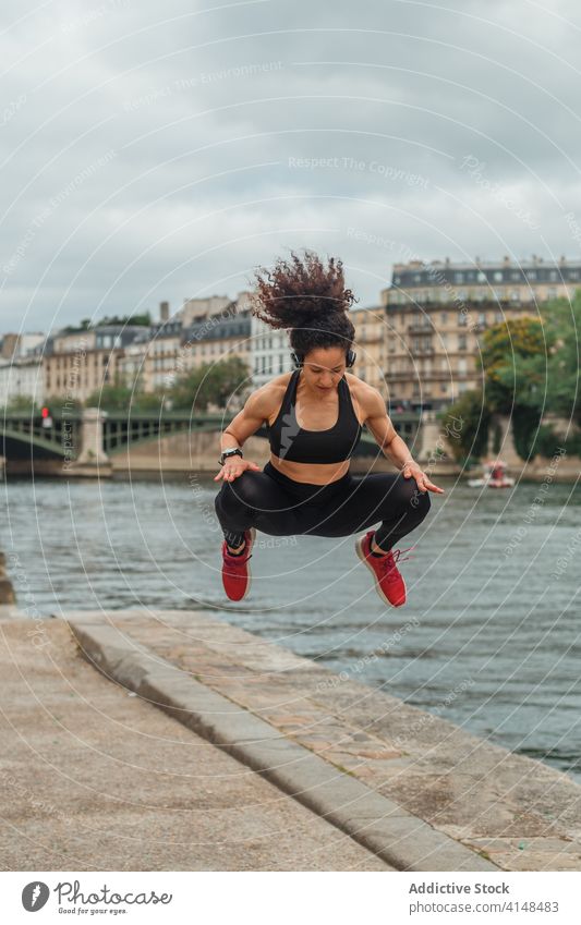 Muskulöse ethnische Sportlerin springt beim Training in der Nähe des Stadtflusses springen Aufwärmen Energie muskulös Fluss Großstadt passen intelligente Uhr
