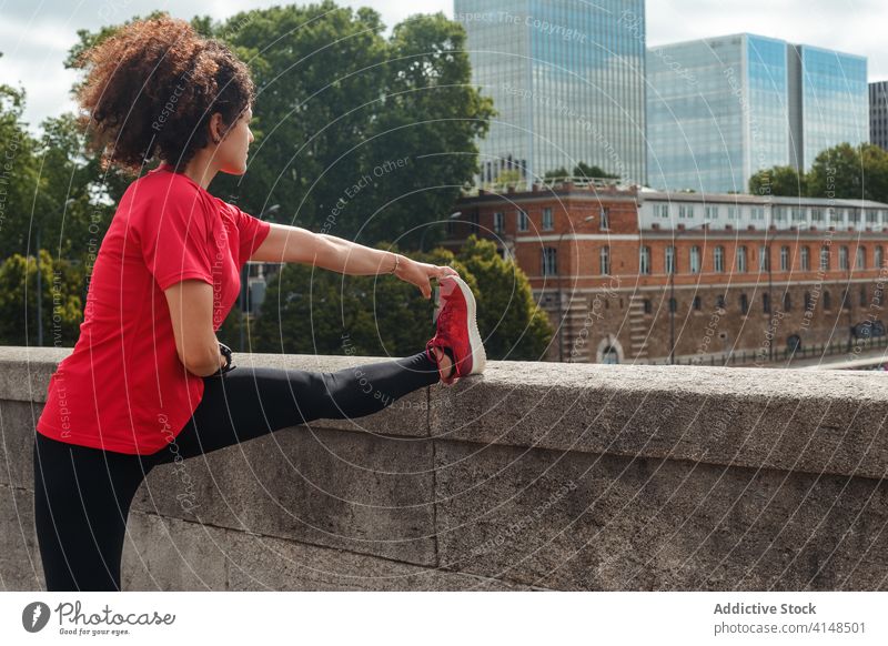 Nicht erkennbarer ethnischer Sportler, der sein Bein beim Training auf der Stadtbrücke streckt Athlet Dehnung Übung beweglich Wohlbefinden Aufwärmen Brücke