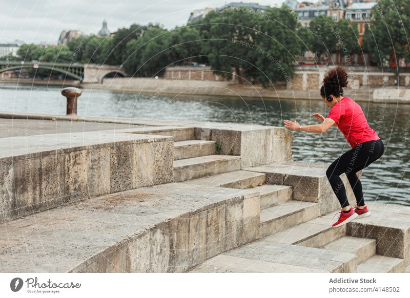 Anonymer ethnischer Sportler springt auf Steintreppe in der Nähe des Stadtteichs Sportlerin springen Training Aufwärmen Energie Sportbekleidung Treppe Fluss