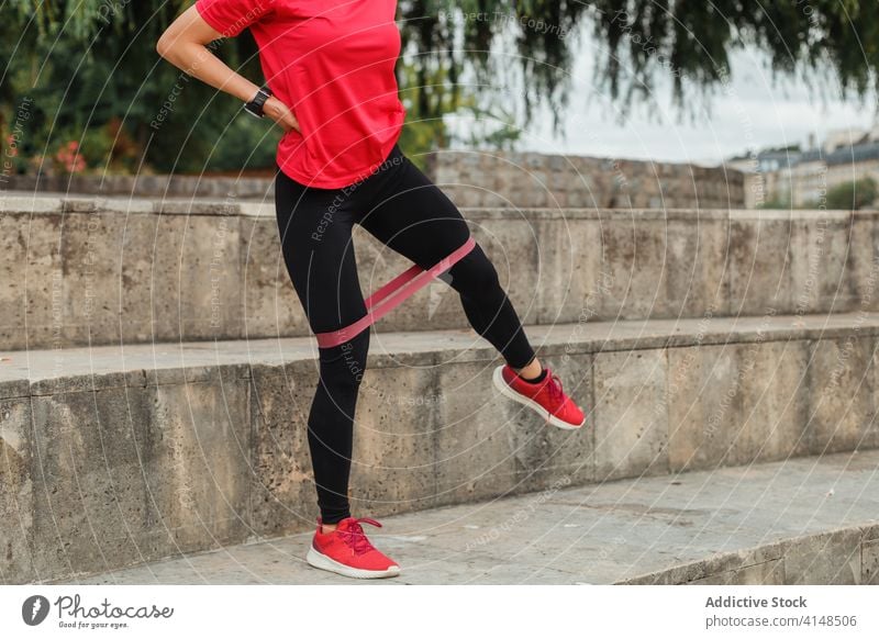 Anonymer Sportler mit intelligenter Uhr beim Hocken mit Gummiband im Freien Sportlerin Kniebeuge Klebeband elastisch Training Übung intelligente Uhr Headset