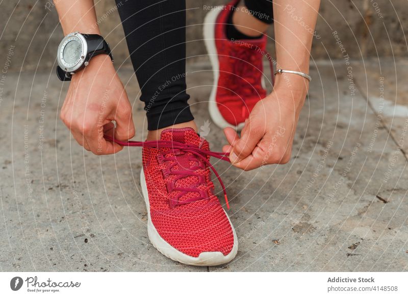Unkenntlich gemachte Sportlerin mit intelligenter Uhr, die die Schnürsenkel ihrer Turnschuhe bindet Krawatte Schuhbänder intelligente Uhr klassisch Kniebeuge