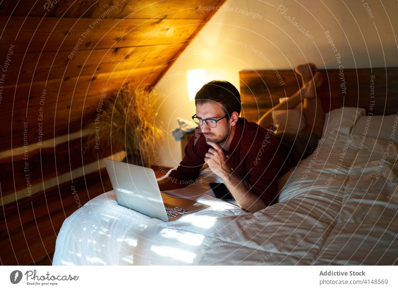 Konzentrierter männlicher Freiberufler, der zu Hause am Laptop tippt Tippen freiberuflich abgelegen Mann Arbeit Projekt Unternehmer benutzend heimwärts Bett