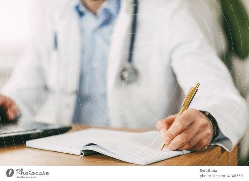 Ein junger Arzt mit orientalischem Aussehen arbeitet, während er mit einem Laptop am Tisch im Netzwerk sitzt und sich Notizen in einem Notizbuch macht Medizin