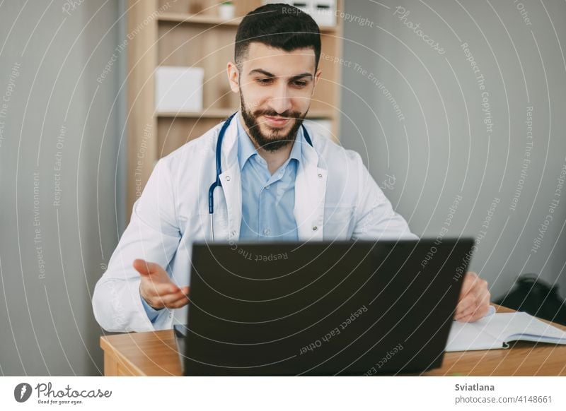 Junger männlicher Arzt, der eine Online-Videokonsultation auf einem Laptop in seinem Büro durchführt geduldig Gesundheit Klinik Stethoskop Therapeut