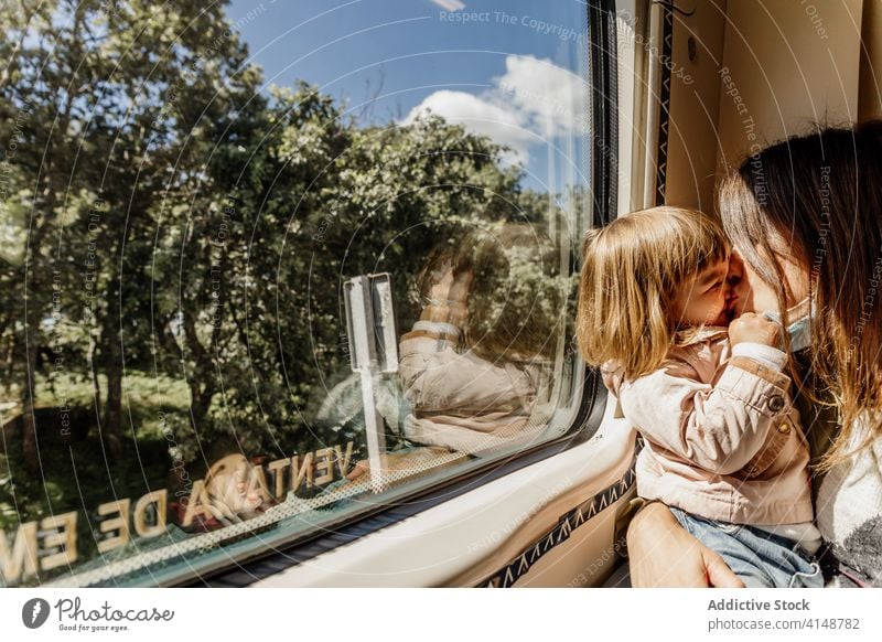 Zufriedene Frau und Kind im Zug reisen Kuss Mutter Coronavirus Mundschutz Zusammensein spielerisch unterhalten Spaß haben Mädchen Freude Kindheit Tochter Eltern