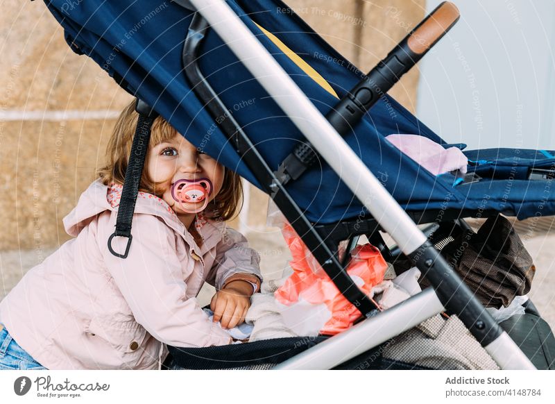 Inhalt kleines Kind in der Nähe von Kinderwagen Baby-Kinderwagen Mädchen Lächeln wenig bezaubernd Straße stehen Wagen niedlich charmant Freude unschuldig Stil