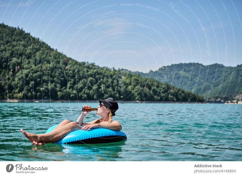 Unbekümmerte Frau in aufblasbarem Ring auf dem See Schwimmer Sommer sich[Akk] entspannen Berge u. Gebirge Urlaub Bier Oberfläche Windstille Wasser sonnig