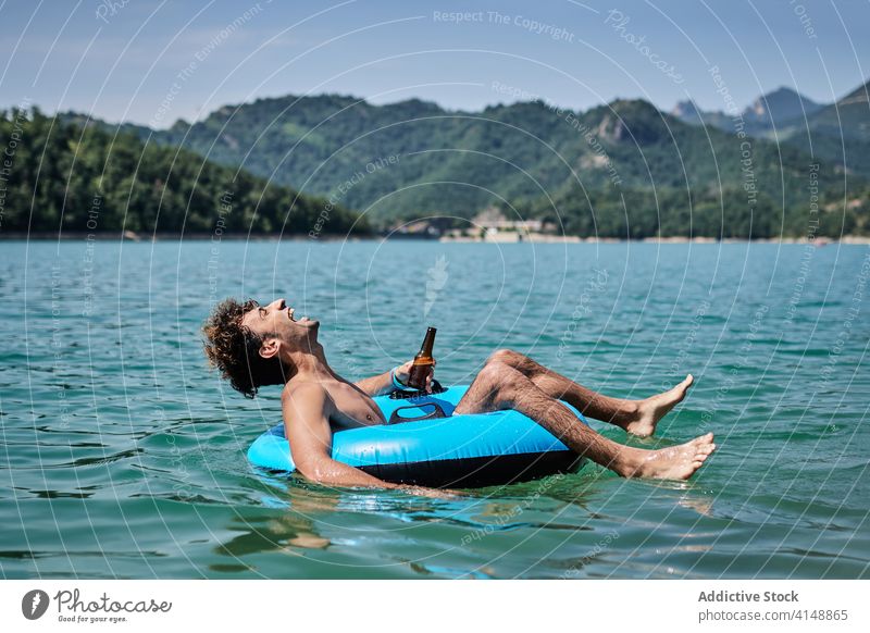 Unbeschwerter Mann in aufblasbarem Ring auf dem See Schwimmer Sommer sich[Akk] entspannen Berge u. Gebirge Urlaub Bier männlich Oberfläche Windstille Wasser