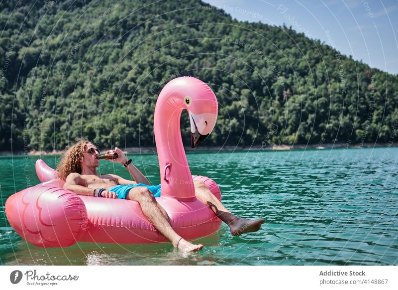 Mann in aufblasbarem Ring auf See sich[Akk] entspannen Schwimmer trinken Alkohol Flamingo Form männlich Lügen Flasche Wasser Feiertag Erholung Sommer Urlaub
