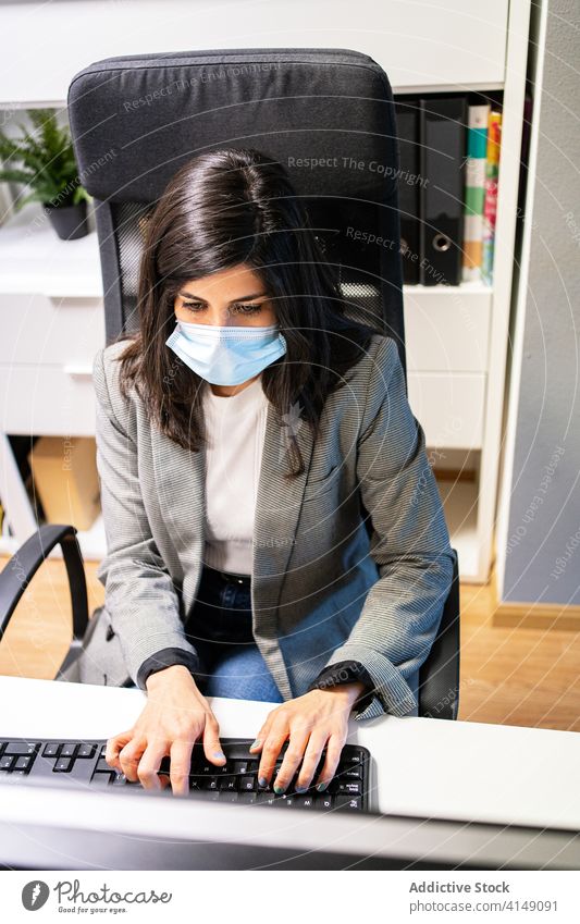 Junge Frau mit medizinischer Maske arbeitet am Computer am Arbeitsplatz Büro Arbeitsbereich benutzend beschäftigt Mundschutz Business behüten Coronavirus