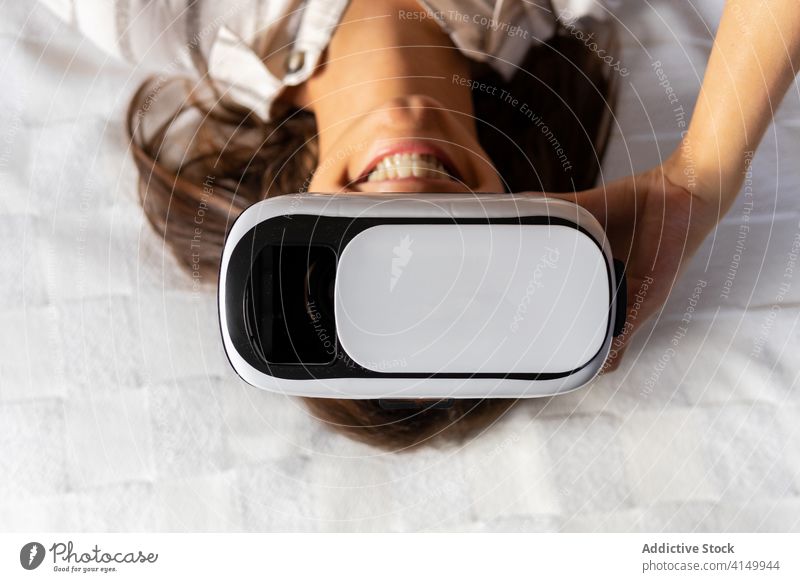 Junge Frau erkundet den Cyberspace auf dem Bett VR Headset erkunden Lächeln gestikulieren ruhen Lügen modern futuristisch Glück Freude Gerät Apparatur heimwärts
