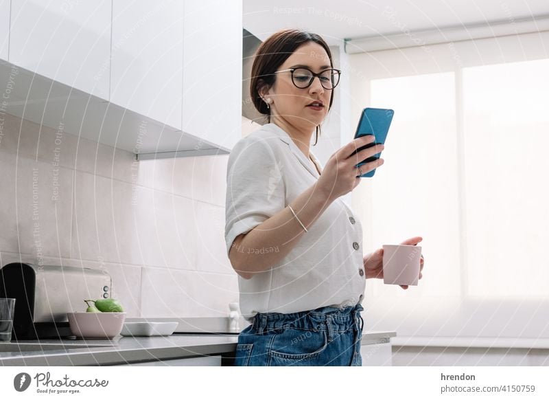 Frau trinkt Kaffee in der Küche, während sie ihr Smartphone benutzt im Innenbereich eine Person Erholung junger Erwachsener Appartement bequem Routine