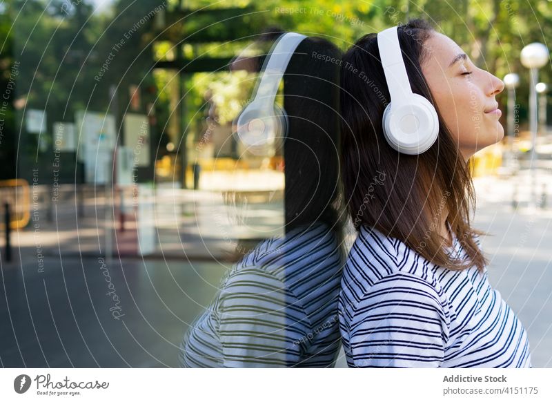 Ruhige Frau beim Musikhören in der Stadt zuhören Kopfhörer genießen Gesang sorgenfrei verträumt zufrieden Großstadt Glaswand Gebäude Spiegel