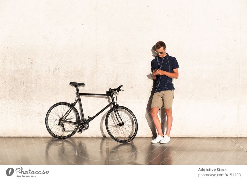 Mann lehnt sich mit dem Smartphone an die Wand Fahrrad blond Business Kaukasier Browsen Handy Mitteilung Textfreiraum Fahrradfahren Radfahrer Unternehmer