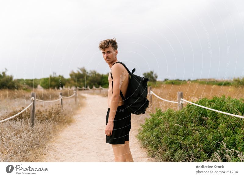 Junger Mann mit Rucksack auf einem ländlichen Weg stehend aktiv ohne Hemd Landschaft jung ernst Feld männlich nackter Torso Natur Sommer Lifestyle Freiheit