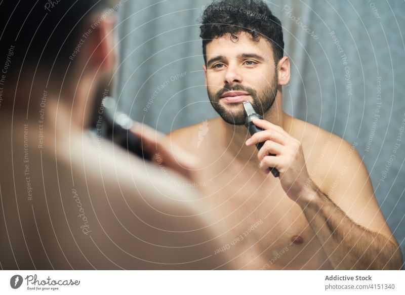 Brutaler Mann rasiert sich zu Hause den Bart mit Trimmer Vollbart Pflege Rasieren brutal Bad heimwärts ernst gutaussehend männlich Konzentration Fokus