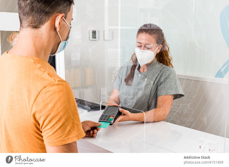 Kunde zahlt mit Kreditkarte in der Klinik Zahlung geduldig Klient Mundschutz Coronavirus neue Normale Terminal bezahlen Dienst elektronisch Gerät Medizin