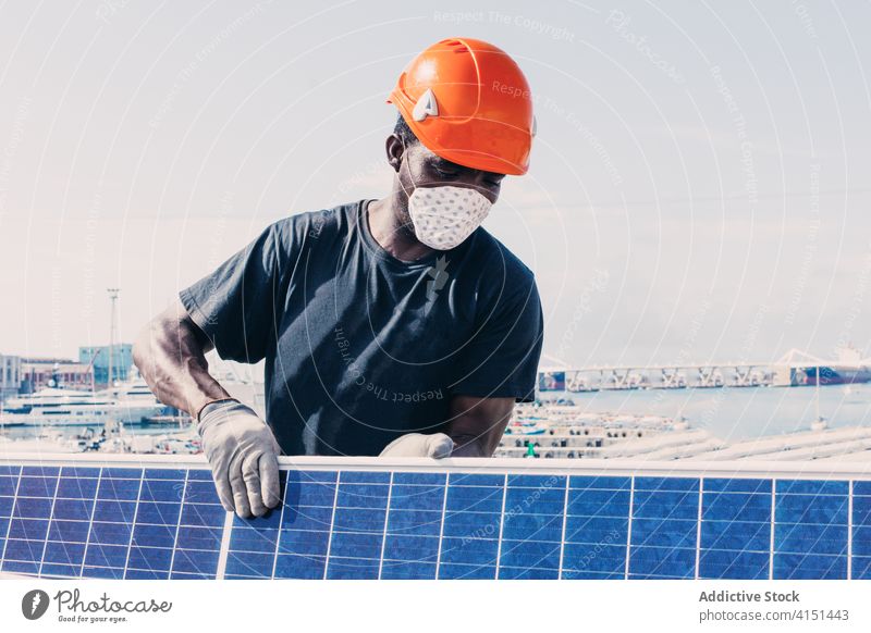 Männlicher Arbeiter mit Maske und Sonnenkollektor solar Panel installieren Batterie Mann Ingenieur alternativ nachhaltig Kraft männlich ethnisch schwarz