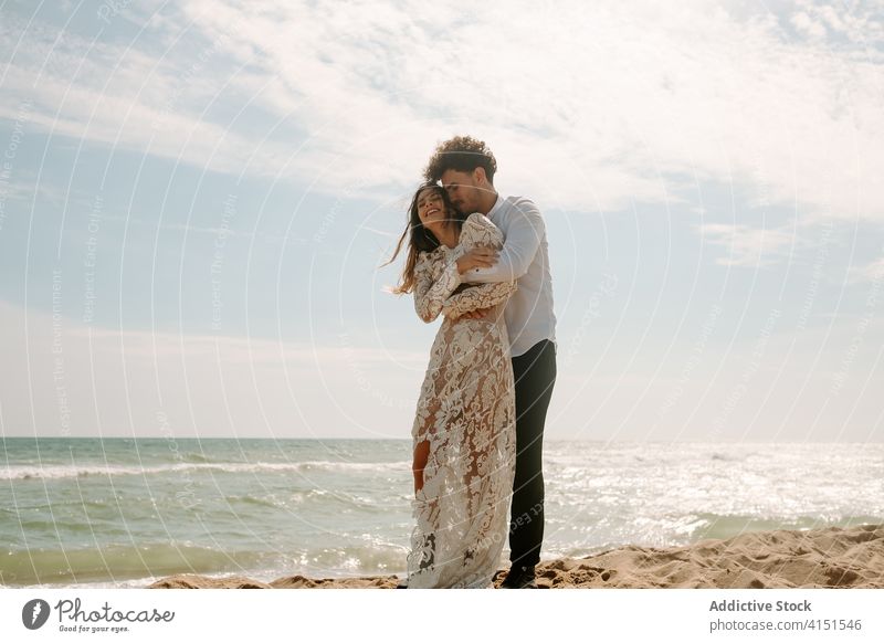 Glückliches frisch verheiratetes Paar steht gegen wogende Meer Jungvermählter Strand romantisch heiter Zusammensein Umarmen Partnerschaft MEER Liebe Natur Sand