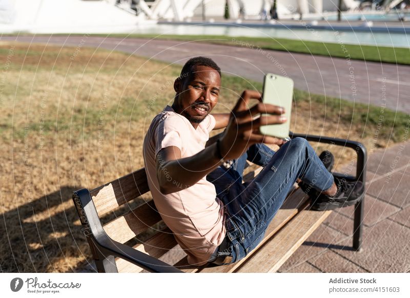 Schwarzer Mann macht Selfie mit Telefon unter Park Bank schwarz Menschen im Freien Smartphone Glück Afroamerikaner Mobile Funktelefon Lächeln Fröhlichkeit