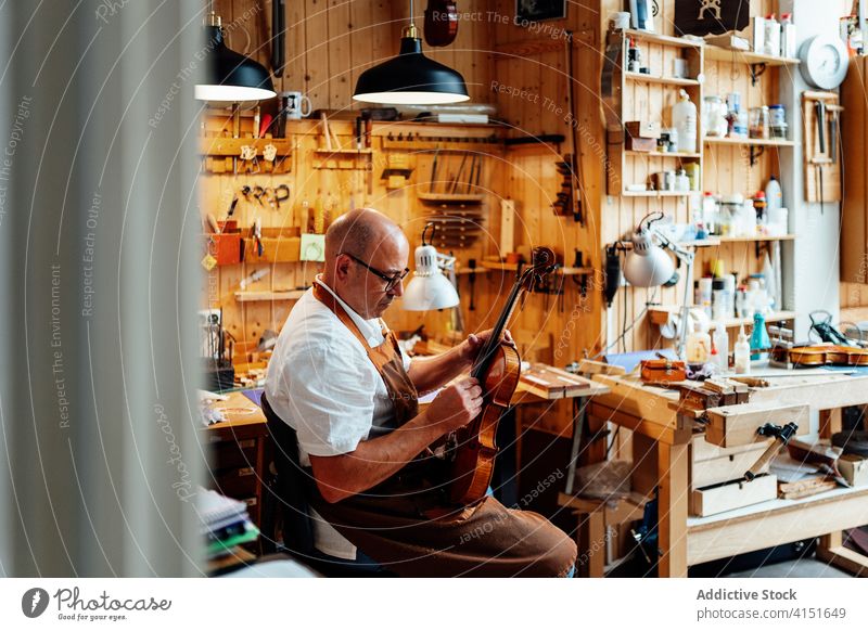 Handwerker mit Geige in professioneller Werkstatt Kunsthandwerker Reparatur Zupfinstrumentenmacher Kunstgewerbler Arbeit Mann wiederherstellen Meister Fähigkeit