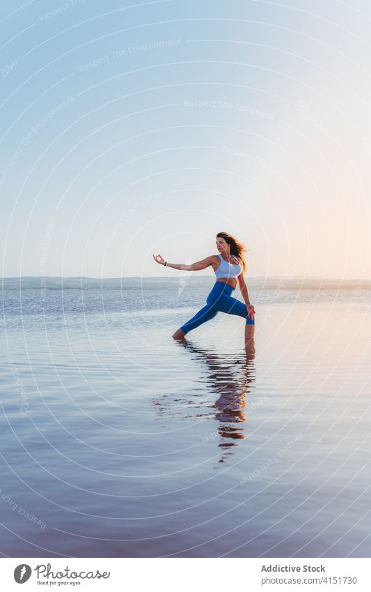 Anmutige Frau in Balance-Yoga-Pose am Seeufer üben Asana stehen halbmondförmiger Ausfallschritt Harmonie Gleichgewicht verdrehen Fokus Wasser Windstille