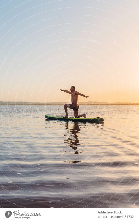 Mann auf Paddelbrett stehend in Yoga-Pose auf See üben Sonnenuntergang Asana halbmondförmiger Ausfallschritt Harmonie anjaneyasana Fokus Wasser Gleichgewicht